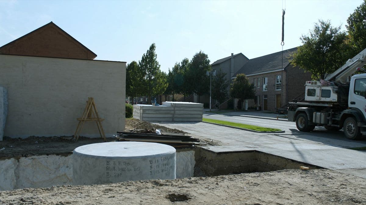 Een Belgische nieuwbouwstraat waar een betonnen regenwaterput in een uitgegraven put wordt geplaatst