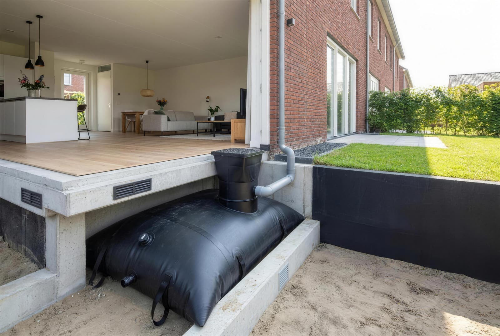 Doorsnede van een woning met een zwarte EPDM waterzak in de kruipruimte onder de vloer, met de schacht en de regenpijpaansluiting